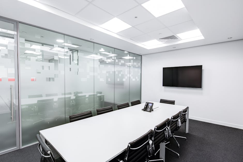 Sleek, minimalist conference room with glass walls, long table, and office chairs.